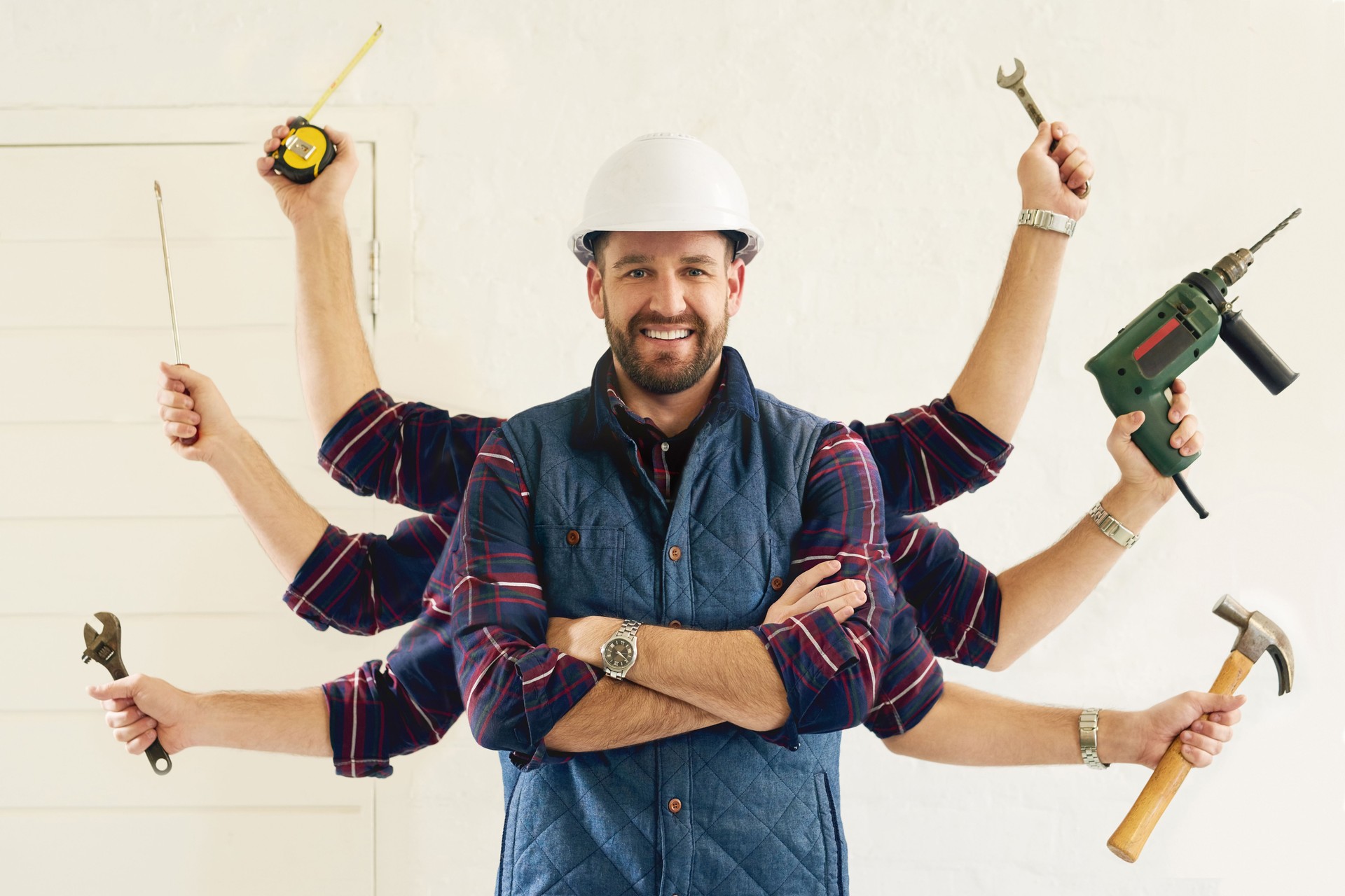 Smiling handyman wearing a white helmet and checkered vest, standing with arms crossed, symbolizing professional and reliable handyman services in London, Milton Keynes, and Northampton.