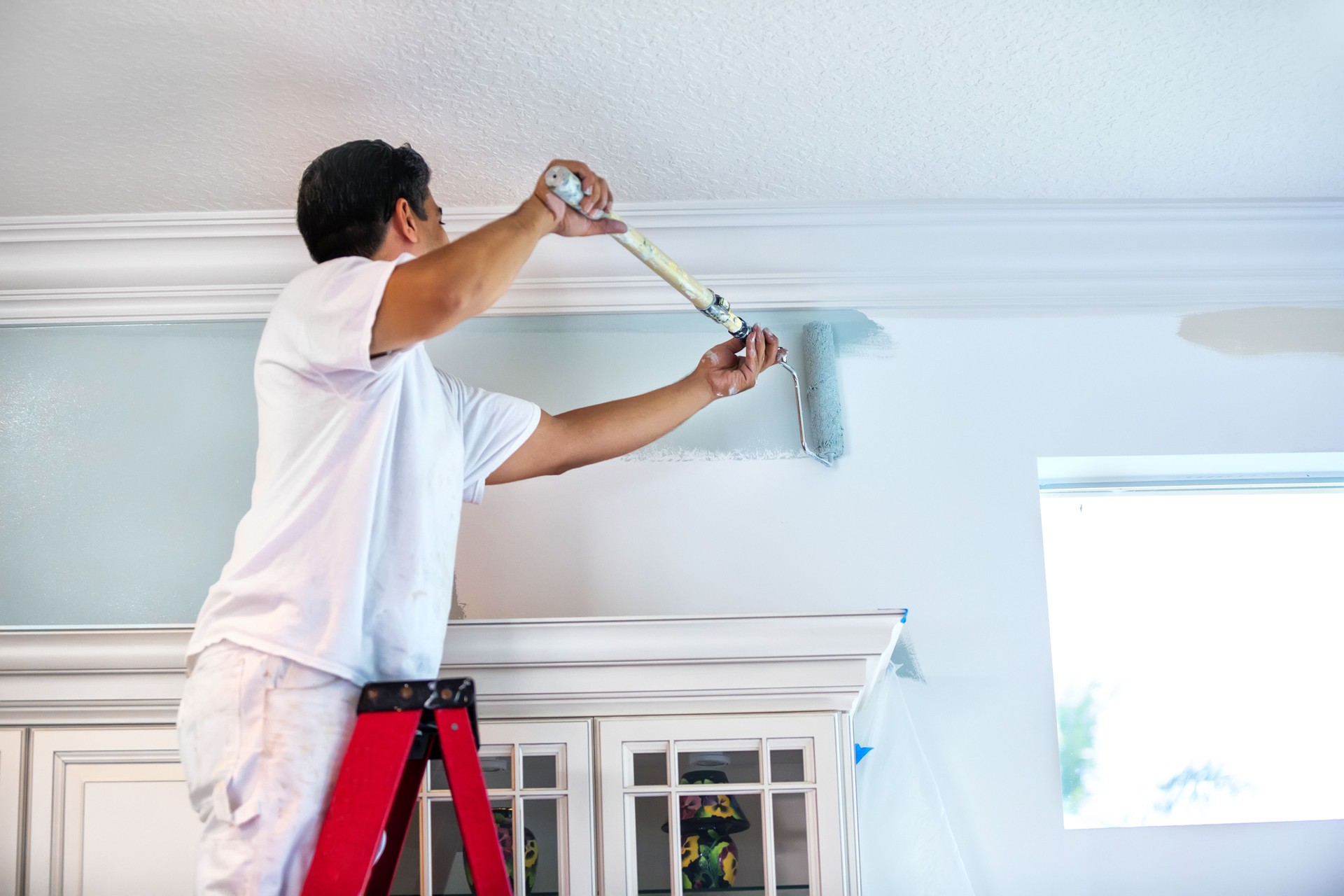 Professional painter on a ladder applying white paint to an interior wall